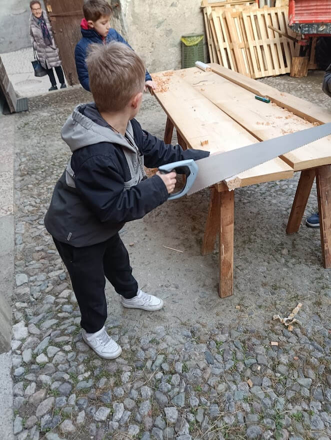 Bambino impegnato a segare assi di legno su banco da lavoro durante un laboratorio pratico.