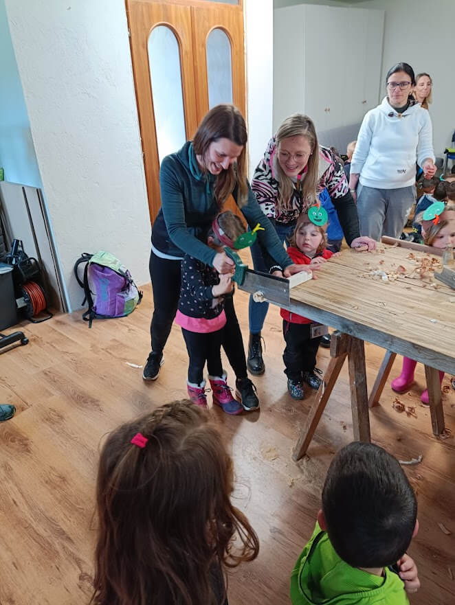 Adulte e bambini piccoli partecipano insieme a un laboratorio del legno con strumenti manuali e guida ravvicinata.