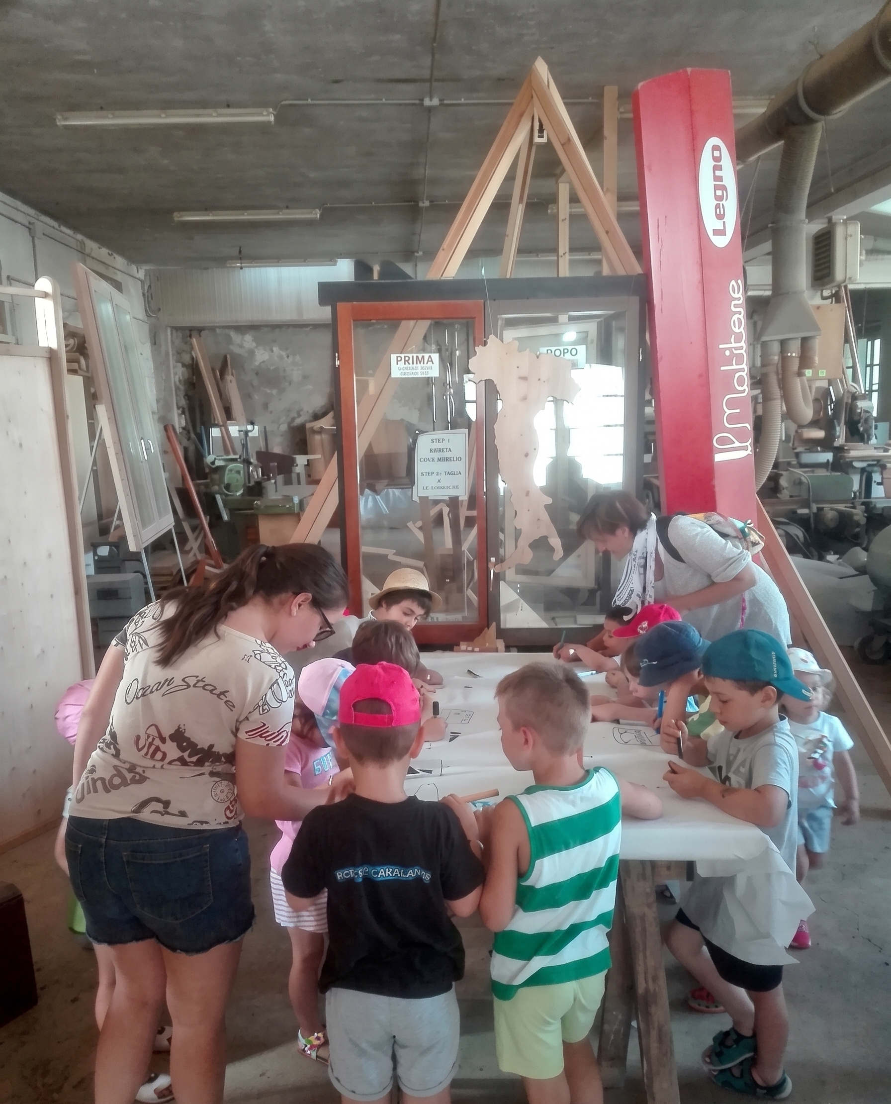 Gruppo di bambini coinvolto in un laboratorio interno attorno a tavoli di lavoro e materiali condivisi.
