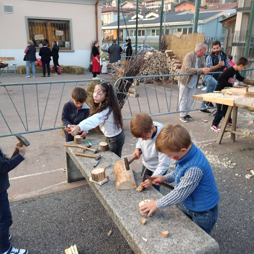 Attivita' collettiva di falegnameria in uno spazio aperto con adulti e bambini attorno ai tavoli di lavoro.