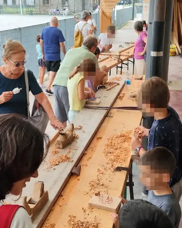 Bambini e adulti lavorano ai due lati di un lungo banco di falegnameria.
