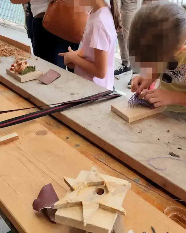 Alcuni bambini costruiscono piccoli manufatti sul banco, tra legni e strumenti.