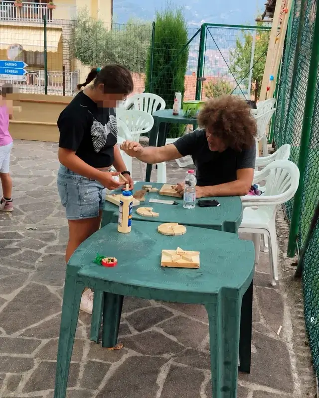 Due partecipanti assemblano piccoli elementi di legno sui tavoli all’aperto.