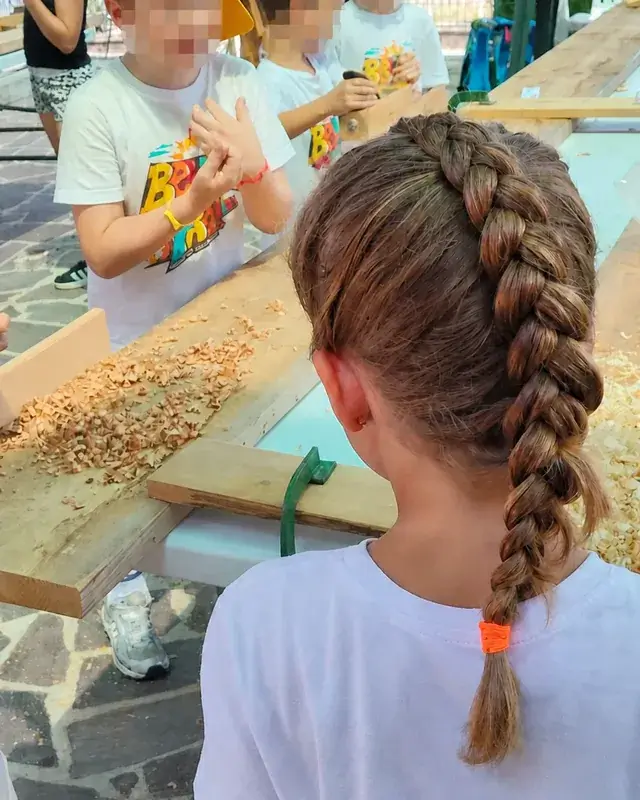 Bambini riuniti al banco tra trucioli, morsetti e utensili manuali.
