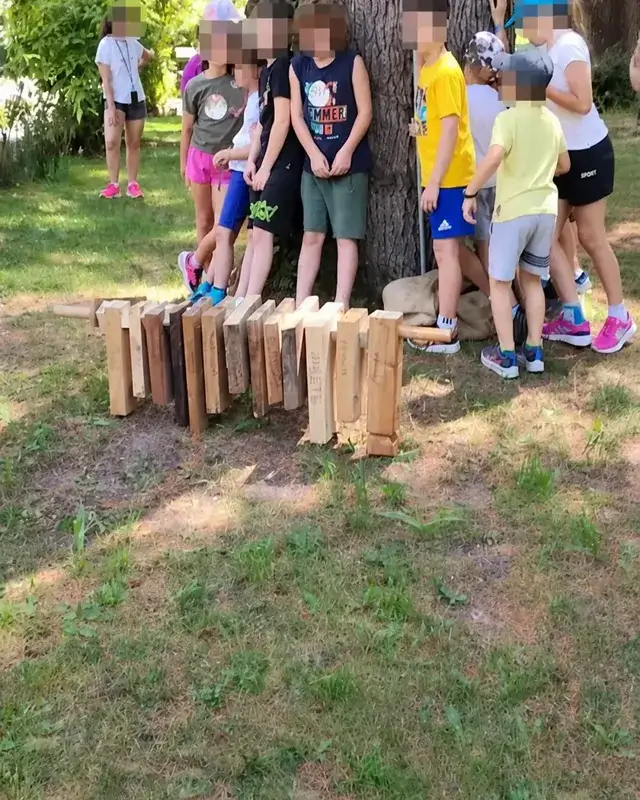 Ragazzi osservano i manufatti di legno disposti sul prato ai piedi di un albero.