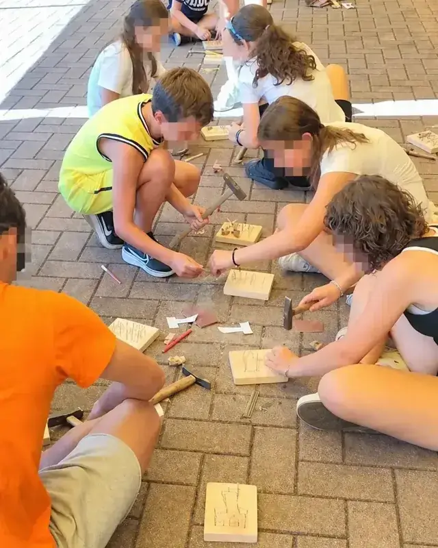 Ragazzi riuniti a terra costruiscono piccoli lavori in legno con martelli e chiodi.