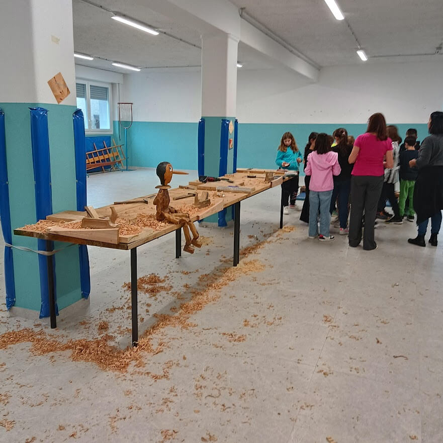 Tavoli di falegnameria preparati con trucioli e manufatti mentre il gruppo si organizza con gli educatori.